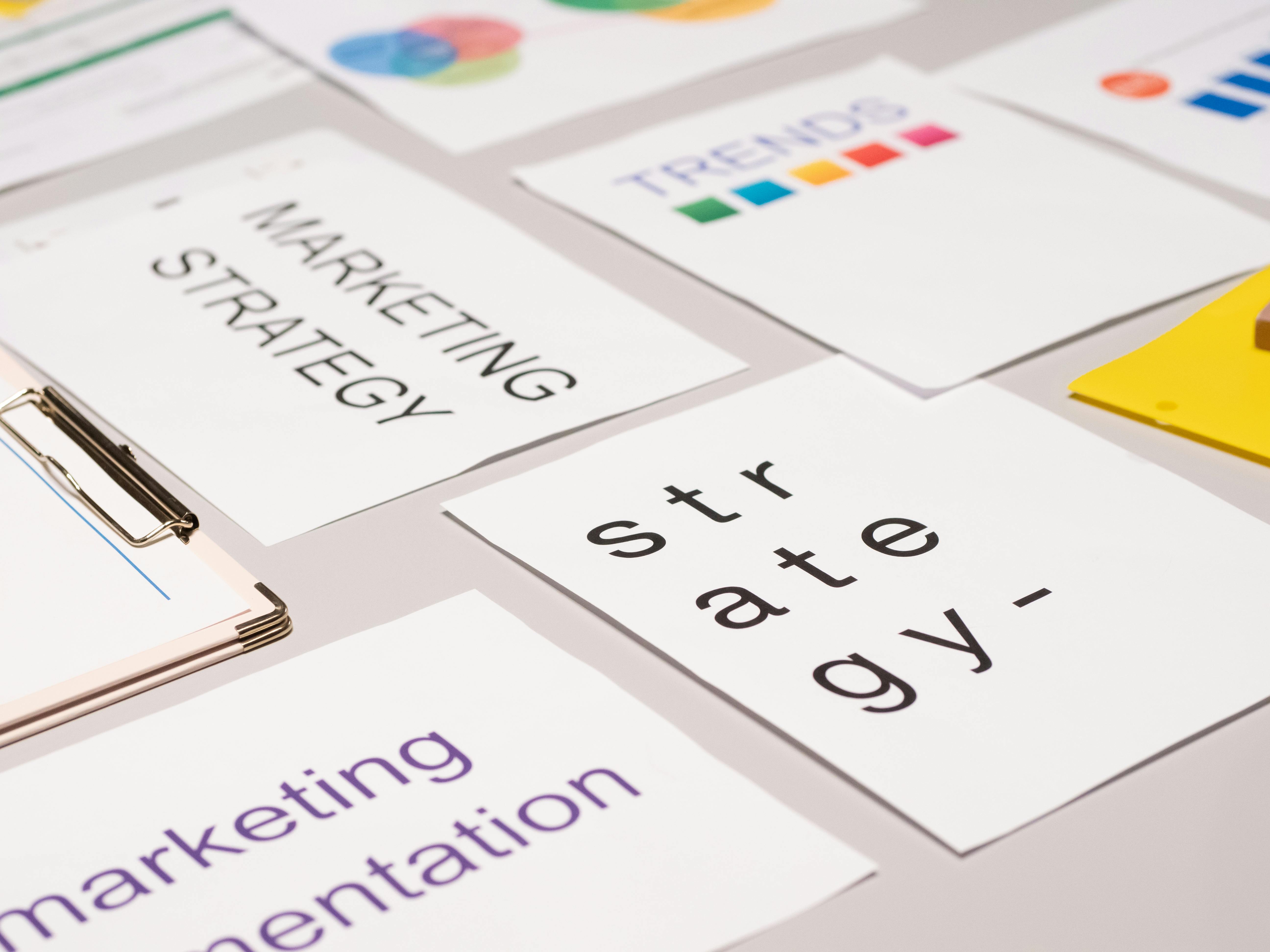 A photograph shows various documents and a clipboard with 'Marketing Strategy', 'Trends', and 'Strategy' on paper on a desk.